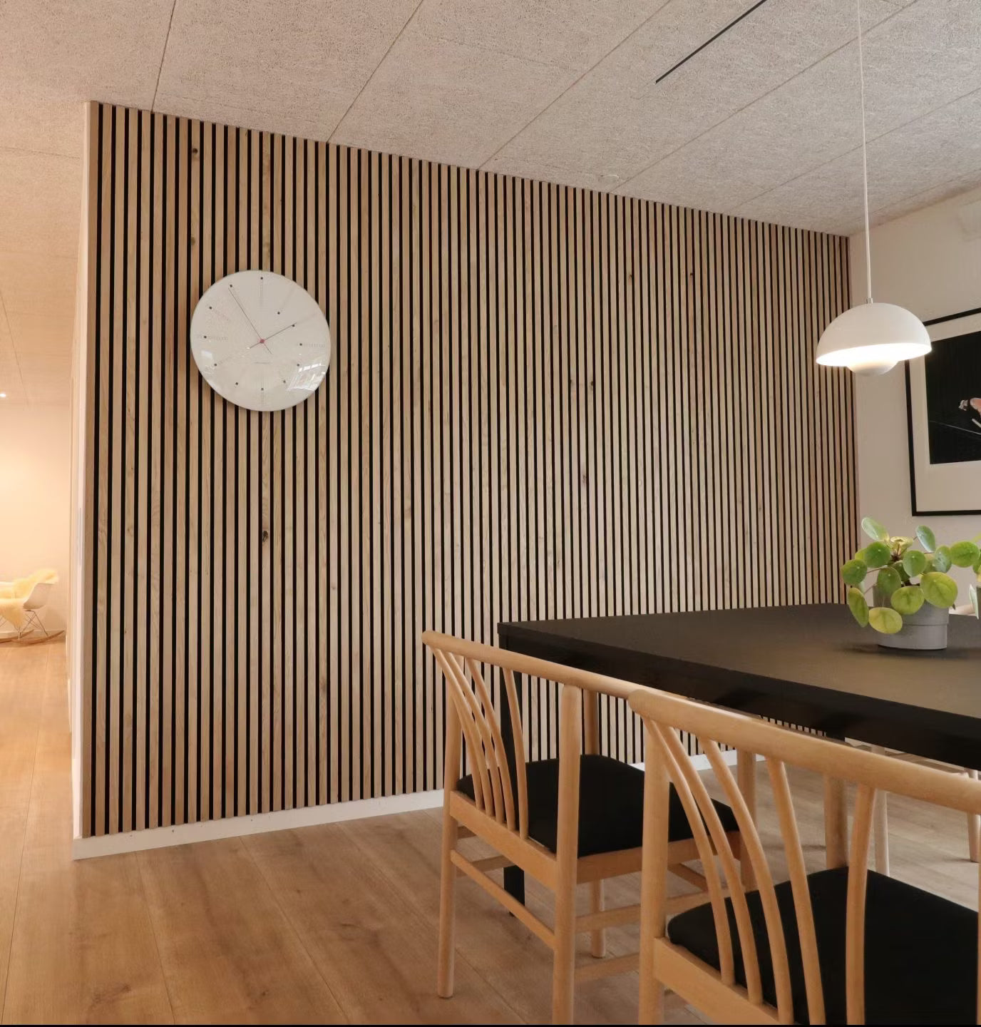 Modernes Esszimmer mit einer Akzentwand aus nordischem Akupanel-Holz, einem schwarzen Tisch, Holzstühlen mit schwarzen Sitzen und einer Topfpflanze als Mittelpunkt.